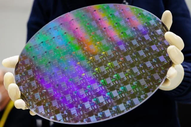 A gloved hand holds a silicon wafer patterned with microchips