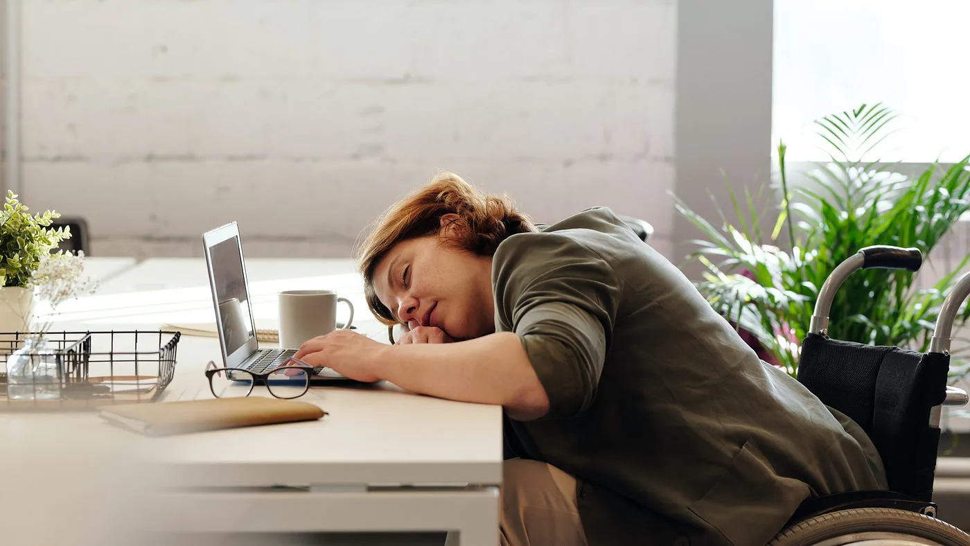 Une personne endormie à son bureau devant un ordinateur portable.