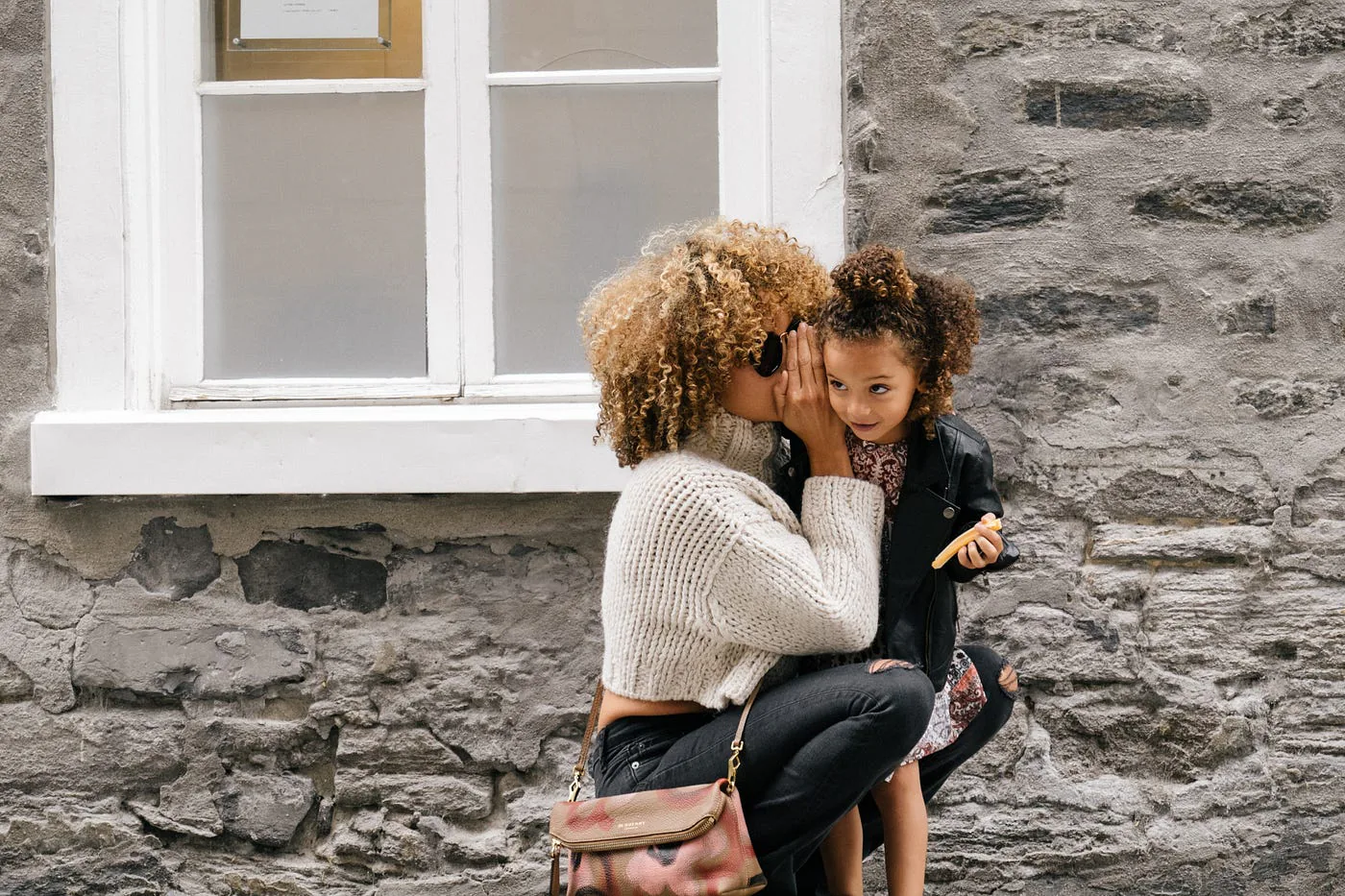 Deux enfants se chuchotent un message devant une maison.